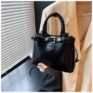 Détail d'un sac à main en cuir noir brillant avec triangle en métal et bandoulière fine