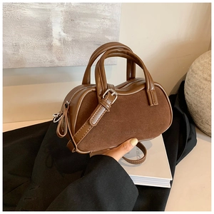 Close-up of matte leather and suede stitching on a dark brown Boston bag held by hand
