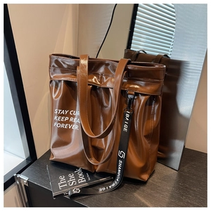 Detail shot of a dark brown glossy leather tote bag with a branded ribbon and printed letters