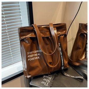 Detail of glossy brown tote bag with white slogan text and decorative lettered strap