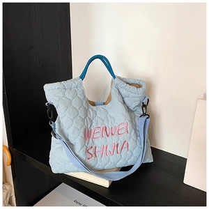 Detail of light blue quilted tote bag with pink embroidery on black and white shelf
