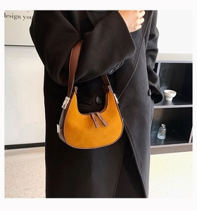 Detailed close-up of yellow suede crescent bag with dark brown leather strap worn by model