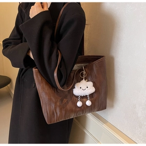Détail d'un cabas marron foncé avec texture bois gaufrée et breloque nuage en peluche