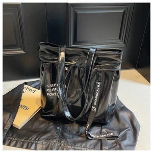 Detail of glossy black tote bag featuring artistic white lettering and a long logo strap