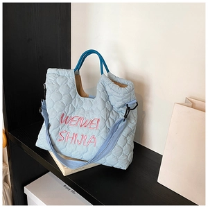 Close-up of light blue quilted tote with pink embroidery and adjustable crossbody strap