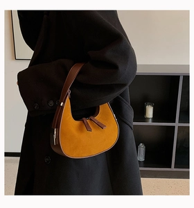 Detail of yellow suede crescent bag with dark brown trim worn with a black wool coat