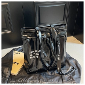 Detail of glossy black leather tote bag with white slogan and decorative strap