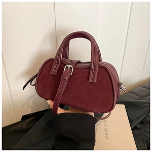 Deep burgundy leather Boston bag with dual handles and adjustable strap in lifestyle setting