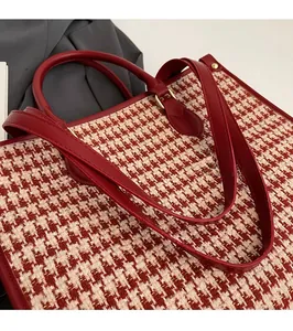 Detail of red tweed tote bag featuring leather handles and adjustable shoulder strap