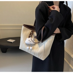 Détail du sac cabas crème à texture ondulée et breloque nuage porté sur un manteau