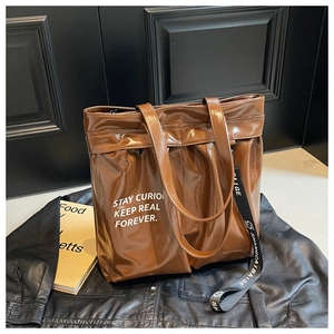 Detail of a brown glossy leather tote bag with white lettering and a black ribbon strap