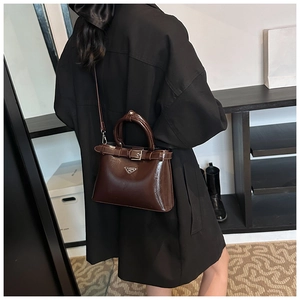 Détail d'un sac bandoulière marron foncé brillant sur un mannequin en manteau noir