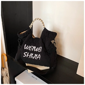 Detail of black quilted tote bag with white embroidery and checkered handles
