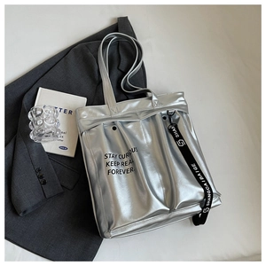 Detail view of metallic silver tote bag with black letter print on a gray suit background