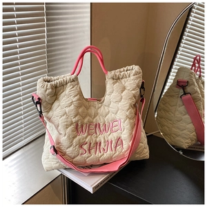 Macro detail of quilted cream tote bag with pink embroidery and metallic side hooks