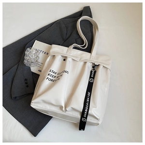 Close-up of cream glossy tote bag with black lettering on grey fabric background