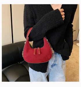 Detail view of a dark red suede crescent-shaped underarm bag shown on a model