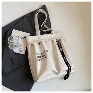 Detail of cream white tote bag featuring black slogan print and branded decorative strap