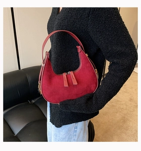 Detail of burgundy hobo bag with matte finish and dual zippers on a model wearing jeans