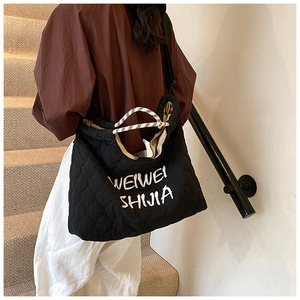 Macro detail of black quilted tote bag featuring white embroidered text and woven straps