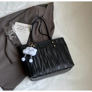 Détail d'un cabas noir avec texture verticale et pendentif en peluche nuage blanc