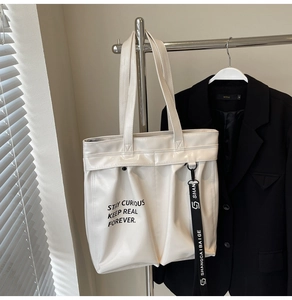 Detail of white PU leather tote bag with black text print and contrast ribbon