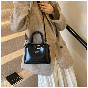Détail du sac à main noir brillant avec plaque triangulaire et bandoulière réglable