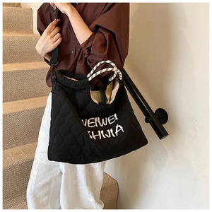 Close-up of black quilted tote bag with embroidery and woven handle shown on model