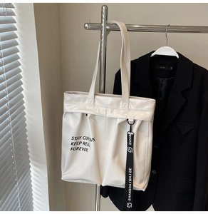 Close-up of glossy off-white tote bag featuring black lettering and stylish charm strap