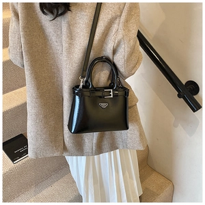 Mannequin portant un sac en cuir verni noir avec boucle argentée et badge métal