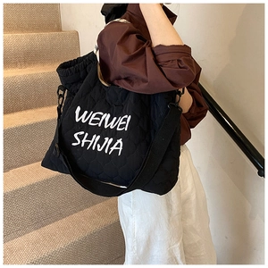 Detailed side view of black quilted tote bag with white lettering and nylon shoulder strap