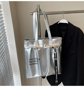 Detail of metallic silver tote bag with decorative logo strap in natural window light