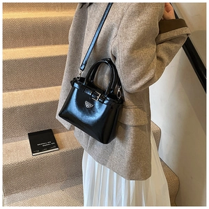 Détail d'un sac à main noir brillant avec logo triangulaire en métal et boucle décorative