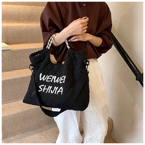 Detail of black quilted tote bag with white lettering and woven handle for daily commute