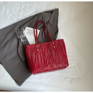 Détail d'un sac cabas rouge en cuir texturé à vagues avec des rivets métalliques dorés