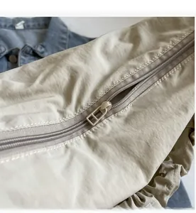 Detail of a smooth color-matched zipper on a lightweight beige nylon shoulder bag