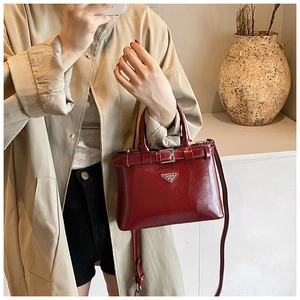 Détail du sac à main en cuir verni rouge foncé avec logo triangulaire et boucle