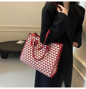Detail of red houndstooth tote bag featuring heart pattern and leather handles with gold rivets