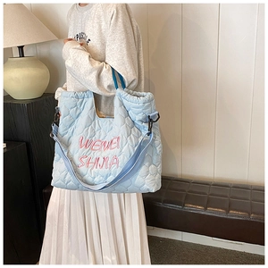 Detailed side view of light blue quilted tote bag with pink embroidery on soft fabric
