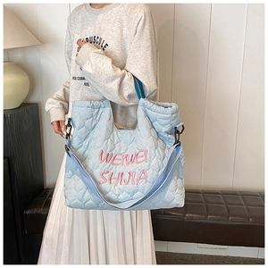 Detailed view of light blue quilted tote bag with pink embroidery and adjustable strap