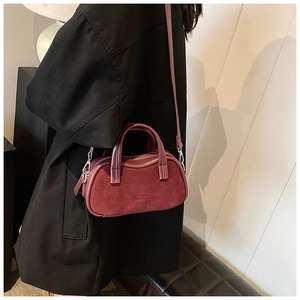Detail of burgundy textured leather crossbody bag with silver hardware on model