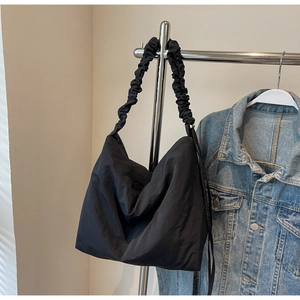 Detail of black tote bag with ruched shoulder strap hanging on a silver metal rack