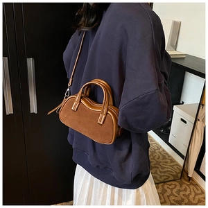 Brown leather crossbody pillow bag shown on a model with blue hoodie and pleated skirt