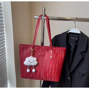 Détail du sac cabas rouge à texture ondulée, accents dorés et breloque nuage sur cintre