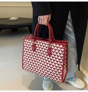 Detail of red heart knit tote bag with premium leather trim and gold metal studs