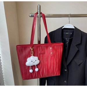 Détail du sac cabas rouge texturé avec pendentif nuage en peluche blanche sur un support