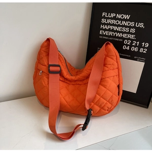 Détail du sac hobo matelassé orange avec large bandoulière sur fond minimaliste