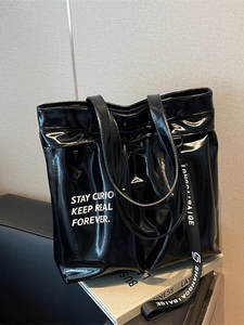 Glossy black patent leather tote bag with white text slogan and decorative logo strap
