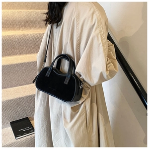 Close-up of a black matte crossbody pillow bag worn with a stylish beige coat on stairs