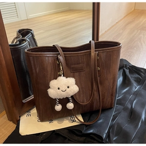 Détail d'un sac cabas marron en similicuir avec un charm en peluche blanc et des lanières